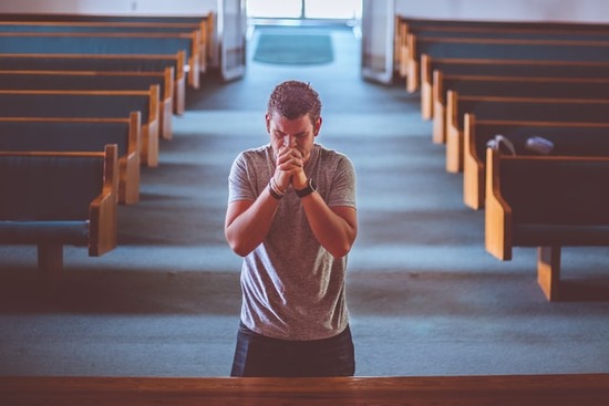 Praying in Church A Christian man kneels at the front of a church to pray