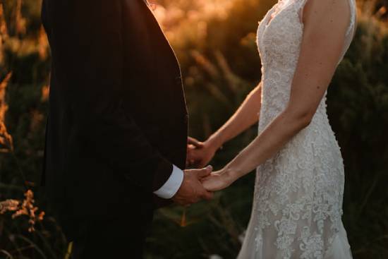 Bride and groom face each other and hold hands as the sun sets A bride and groom face each other and hold hands, depicting oneness in a marriage.