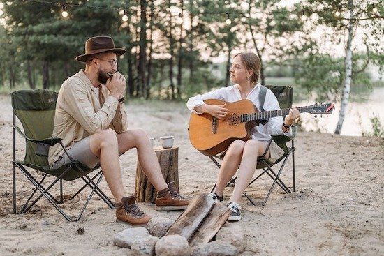 Playing Instruments Camping A man playing a harmonica and a woman playing a guitar by a campfire