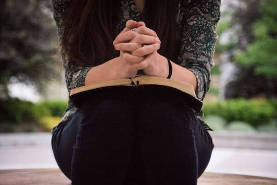 Faith Woman Reading Bible A woman with hands folded on top of a Bible