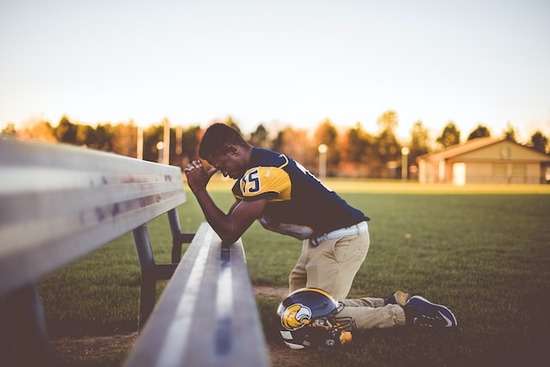 Football Player Praying Football player kneeling down in prayer as we learn where we should pray and that we can anywhere and anytime