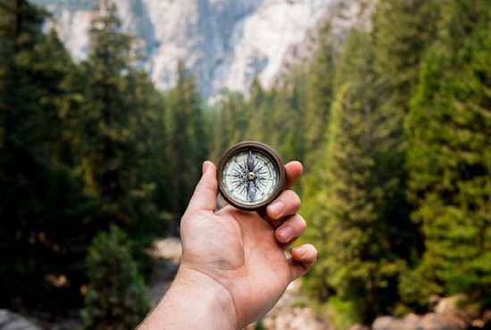 Hand holding a compass in the forest to help guide A person holding up a compass, symbolic of how sola scriptura can guide out beliefs