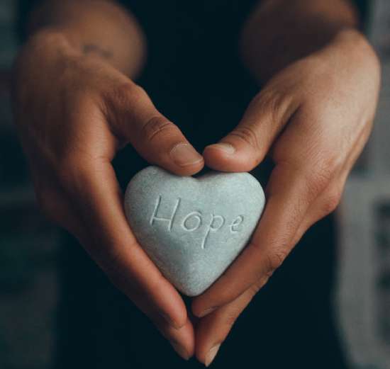 Hands holding a heart-shaped rock with the word Hope etched into it