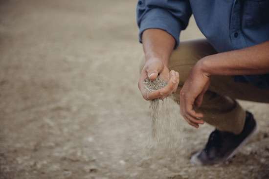 Man sifting sand A man crouching down and sifting dirt through his hands