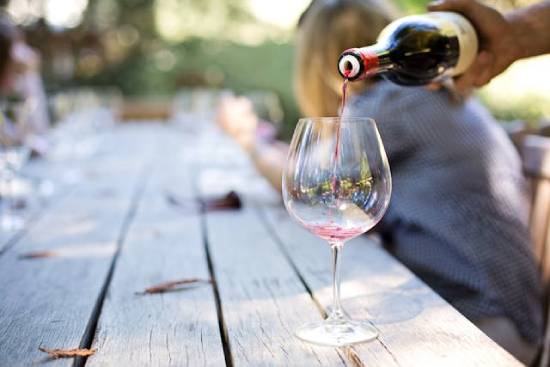 A person pours red wine into a glass. Wine in the Bible can symbolize false teachings and clouded judgment.