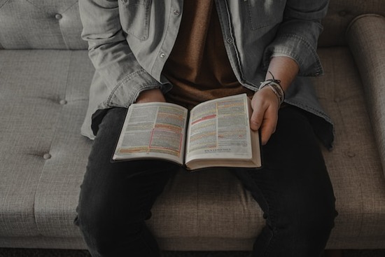 Reading Bible on Couch Sitting down with the Bible will help us better understand God's grace and love.