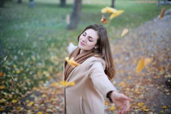 Mental rejuvenation A woman stands, with arms outstretched on an outdoor walkway. Yellow autumn leaves float around her.