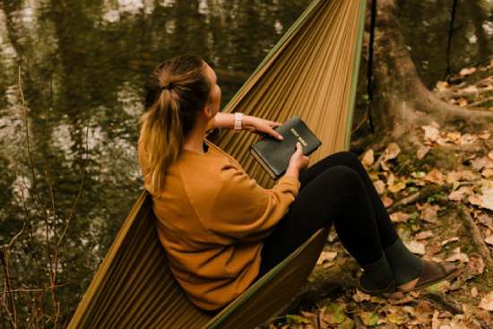 A Woman in brown sweater doing self-reflection A woman sitting in a hammock, contemplating what she just read in her Bible