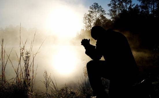 Silhouette of a Man Praying in the Fog  A man kneeling in prayer beside a foggy lake.