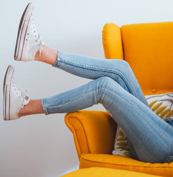 Woman wearing skinny jeans while sitting on orange armchair A woman kicks her legs kicked over the side of an orange chair while wearing skinny jeans and white shoes, which represents how clothing should enhance, and not harm, our health.