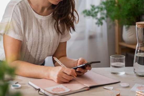 Woman Calendar Planning Ahead  A woman looking at her phone and writing down plans in her calendar so she is prepared for the Sabbath