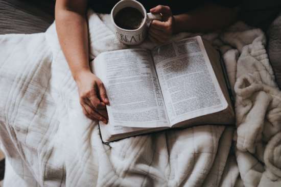 Woman Drinking Tea Reading Bible A person holding a mug of tea and reading the Bible while snuggled up in a blanket