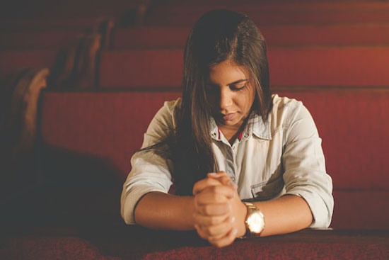 Woman Praying A girl sitting in a church pew, folding her hands and closing her eyes in prayer.