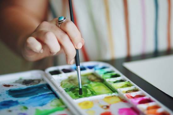 Woman using watercolor paints A woman's hand dips a small paintbrush into a paint palette.