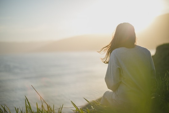 Woman Contemplating A woman sitting on a hill and looking out on the ocean